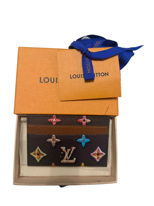 Louis Vuitton wallet with decorative patterns in an open box on a textured surface